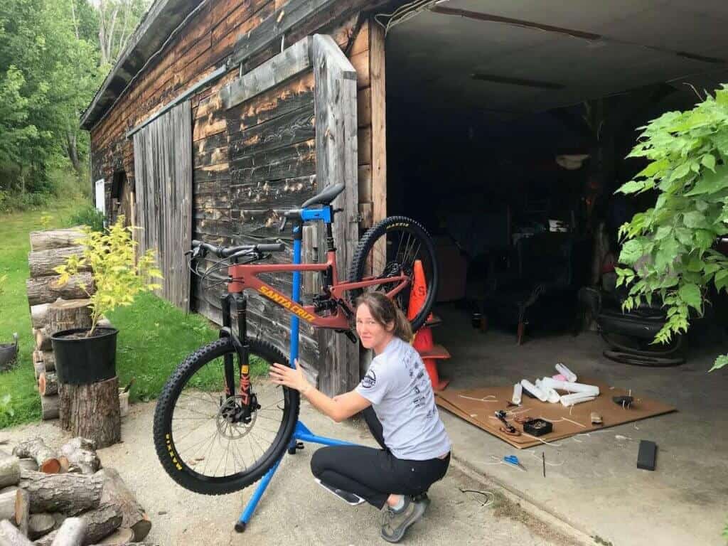 Becky squatting in front of mountain bike on stand outside of garage