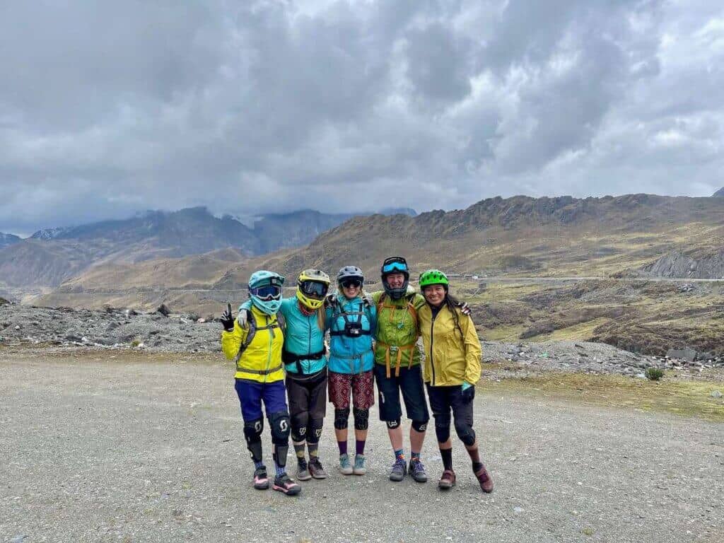 Five women mountain bikers in a line next to each posing for photo at top of mountain in Peru