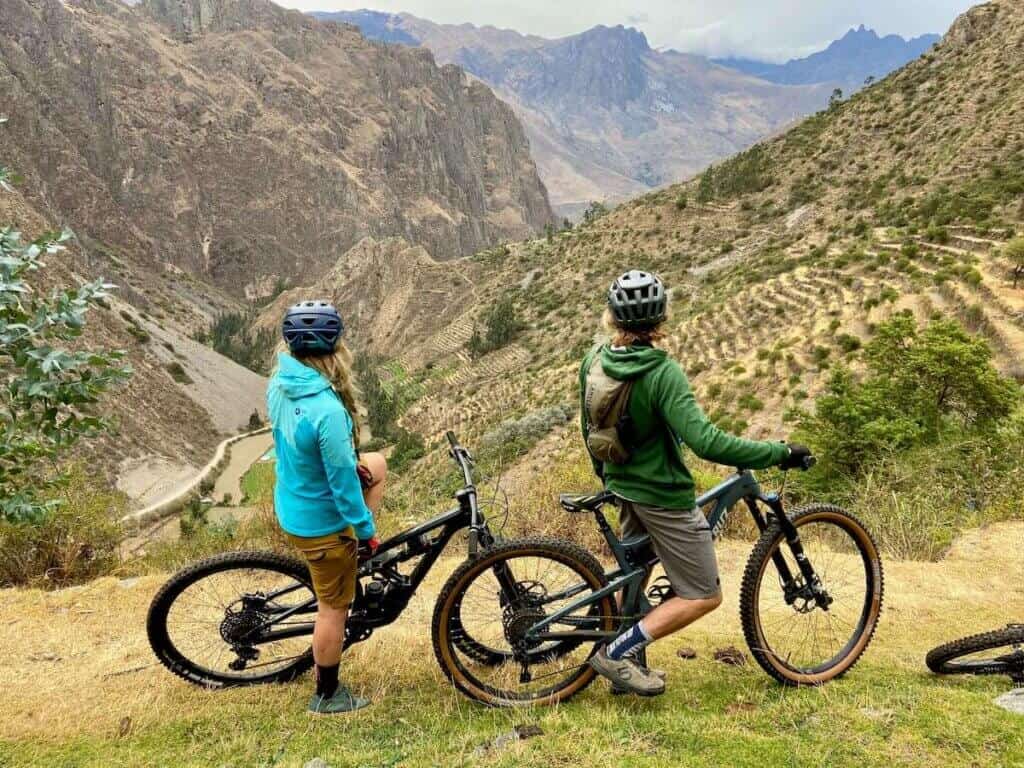 Two mountain bikers stopped on trail in Peru looking out over terraced valley and mountains