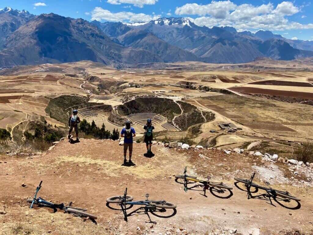 Mountain bikers off bike taking photos of ancient Inca ruin with dramatic mountains in backround in Peru