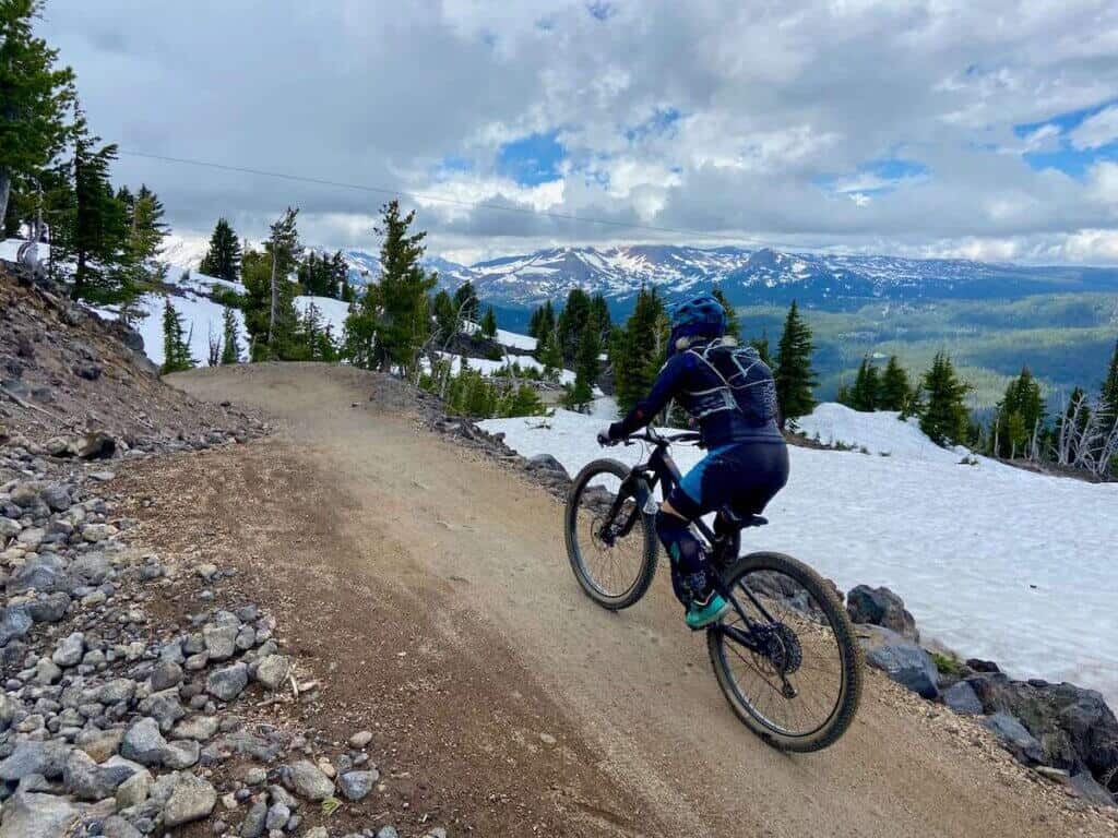 Mountain biker riding bike down singletrack trail at Mt. Bachelor Bike Park in Bend with snow band on righthand side