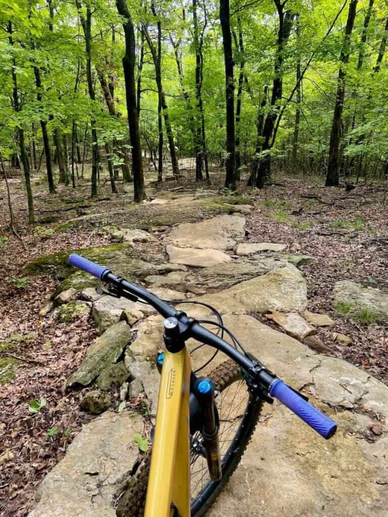 Image out over front handlebars of mountain bike of trail made out of large, flat rocks