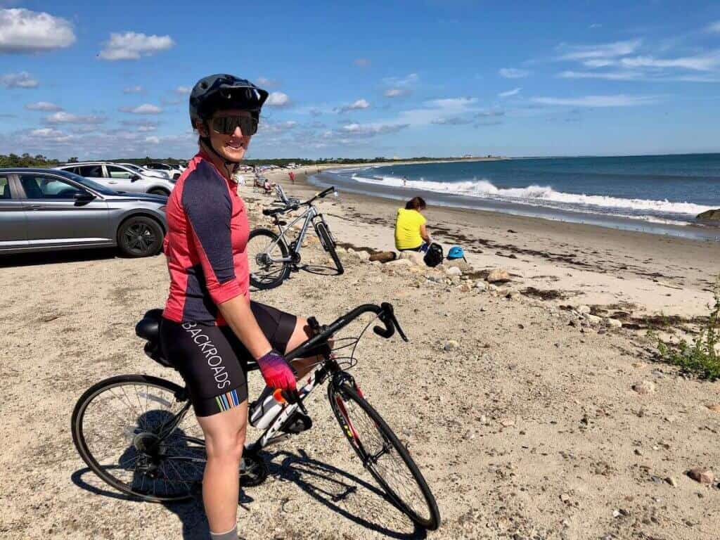 Becky smiling for the camera on road bike at beach in Rhode Island overlooking the ocean