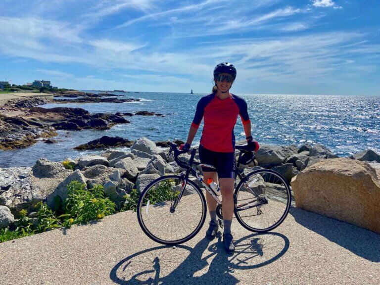 Becky standing next to road bike with coastal Rhode Island ocean views in background