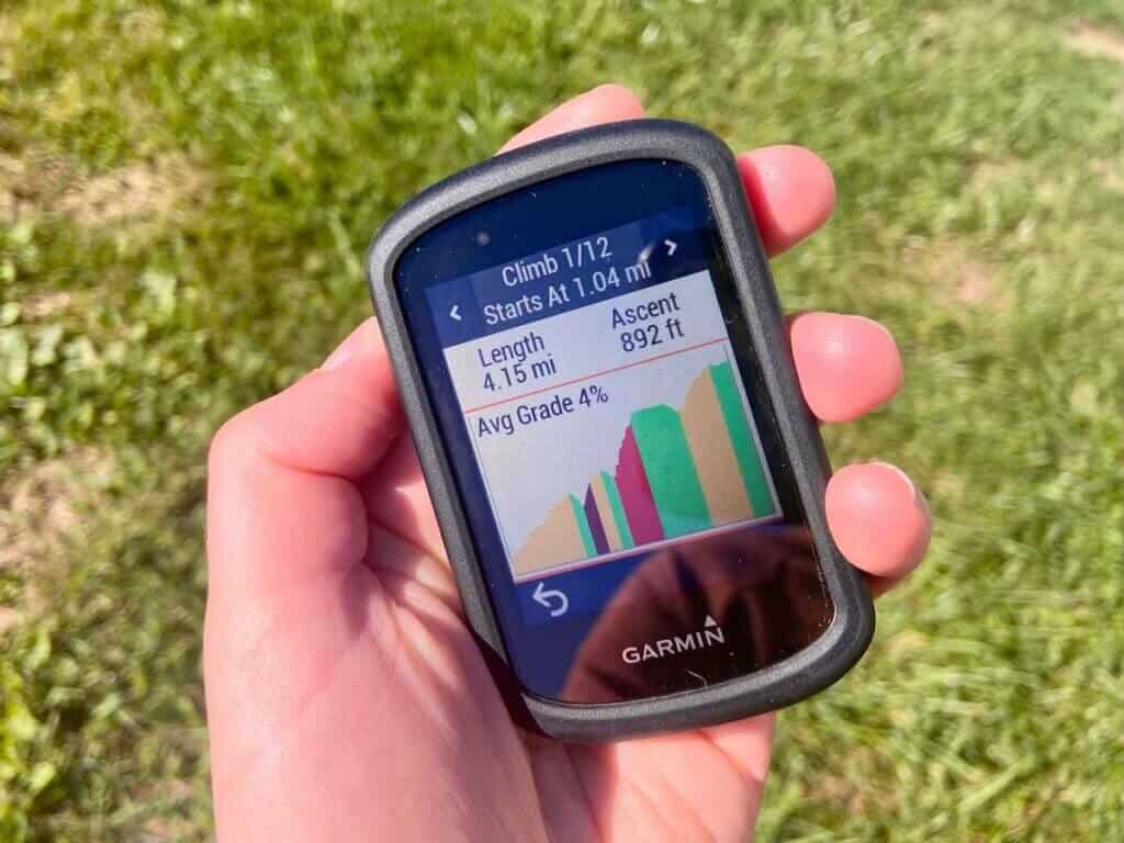 Close up of hand holding Garmin Edge 830 bike computer with screen on ClimbPro which shows average grade, mileage, and ascent of upcoming climb