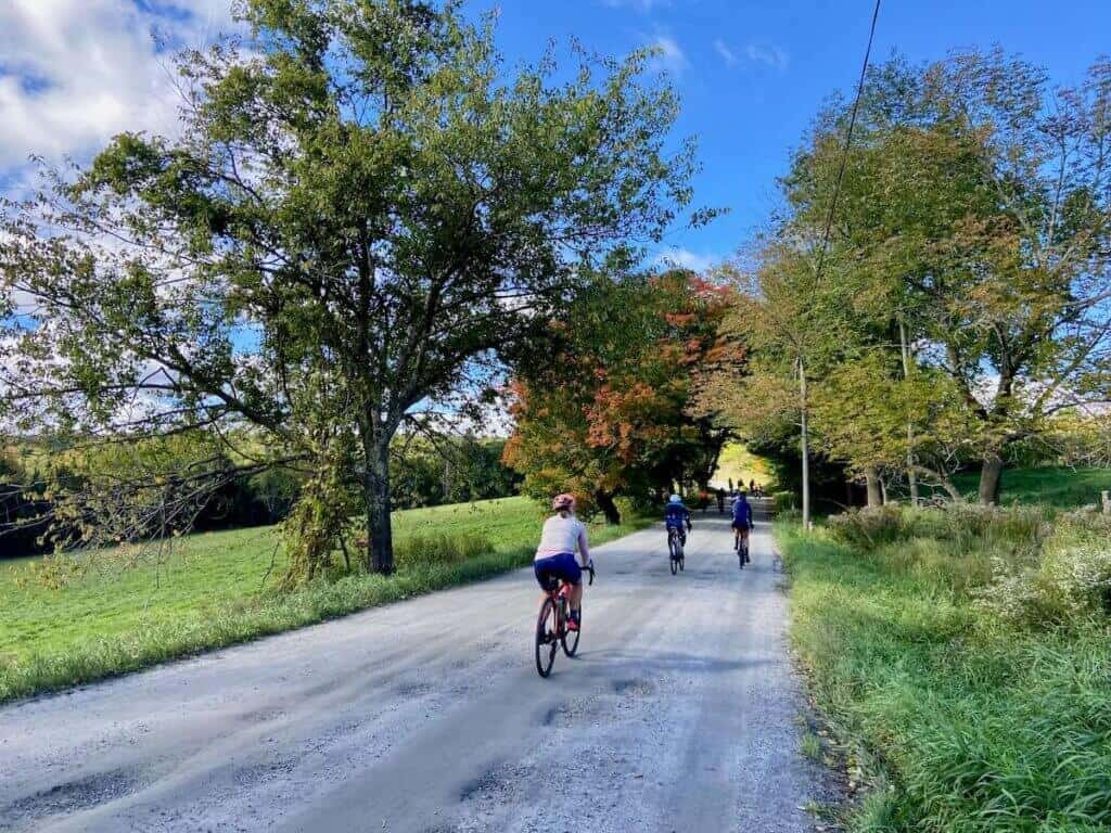 Gravel cyclist riding down dirt road in vermont lined with fall foliage trees