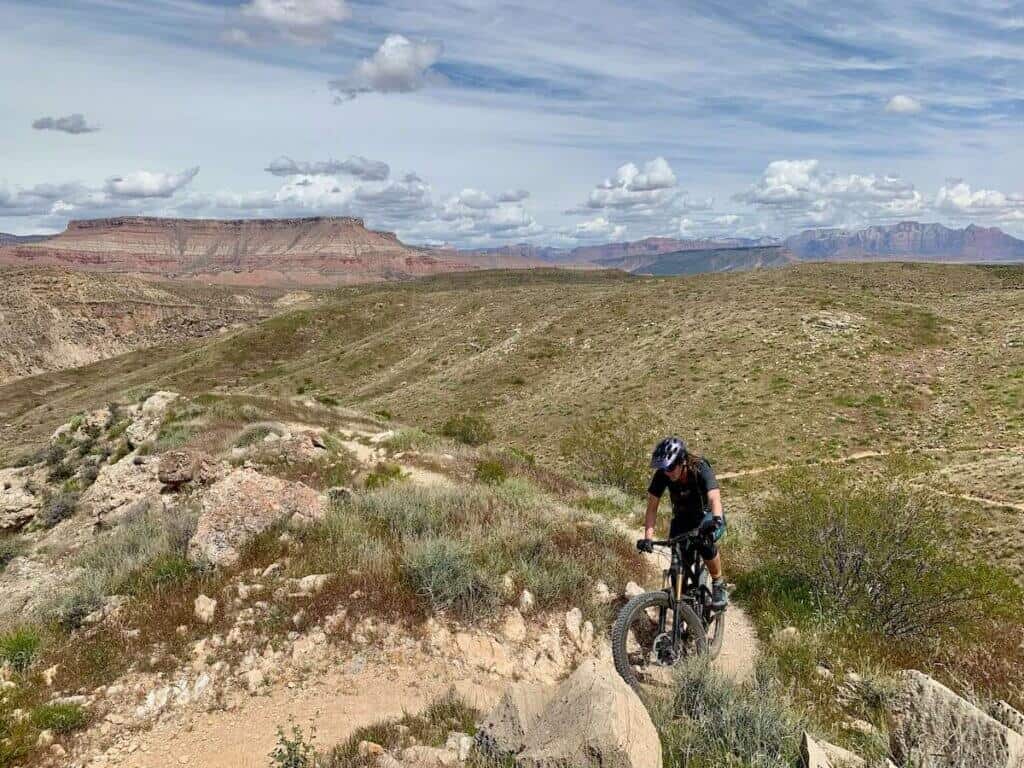 Mountain biker climbing steep hill on bike with Utah mountains and red rock bluffs in background
