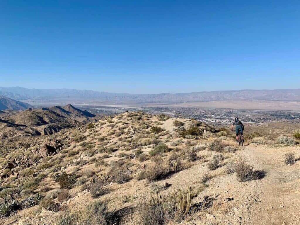 Mountain biker riding down singletrack ridge above Palm Springs California with views of mountainous desert landscape