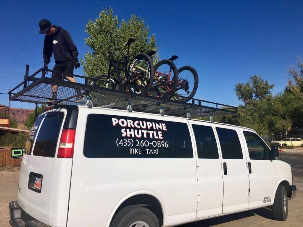 Person on top of van loading mountain bikes into rack. Porcupine Shuttle sticker on window
