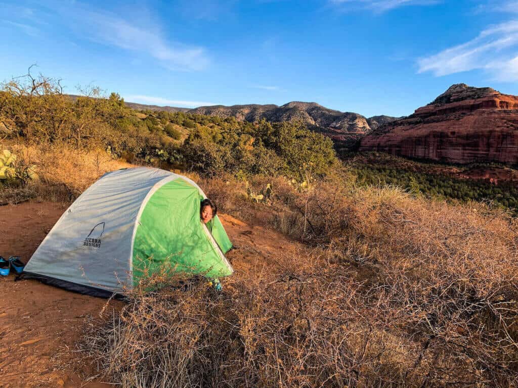 Camper peeking her head out of tent in morning with Sedona red rock cliffs in background