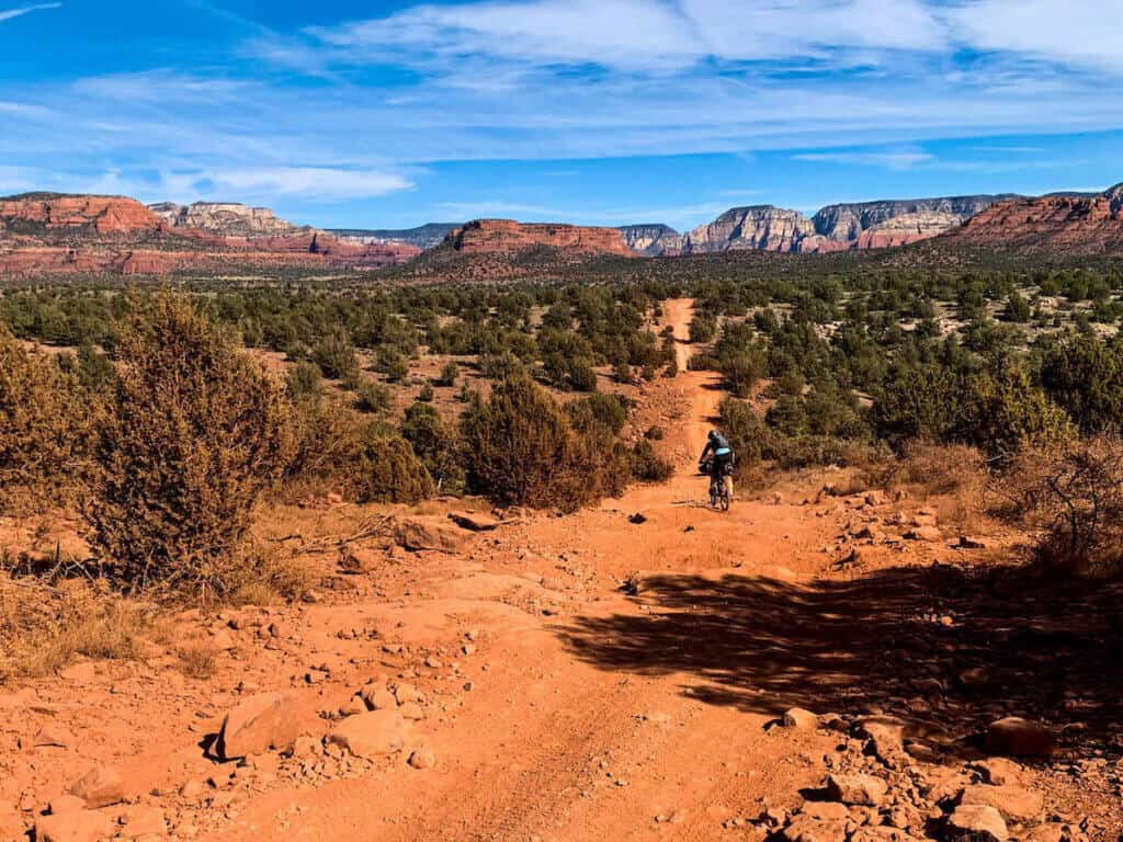 Mountain biker descending rough OVH trail on bike in Sedona with red rock bluffs in distance
