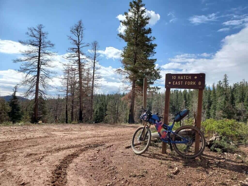 Loaded bikepacking bike propped up next to sign indicating Hatch 10 miles to the right and East Fork 6 miles to the left