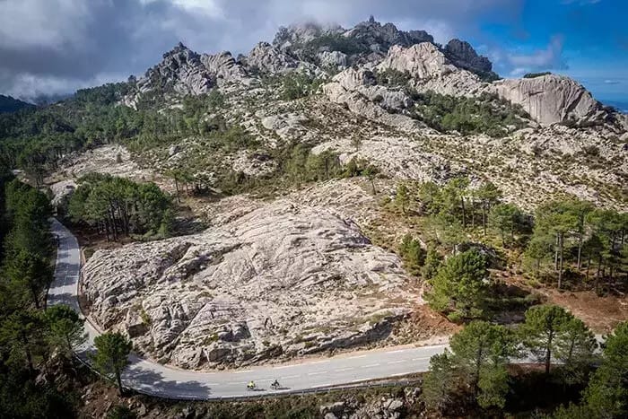 Birdseye view of cyclists on a road winding its way around a rocky mountain peak on Sardinia, Italy