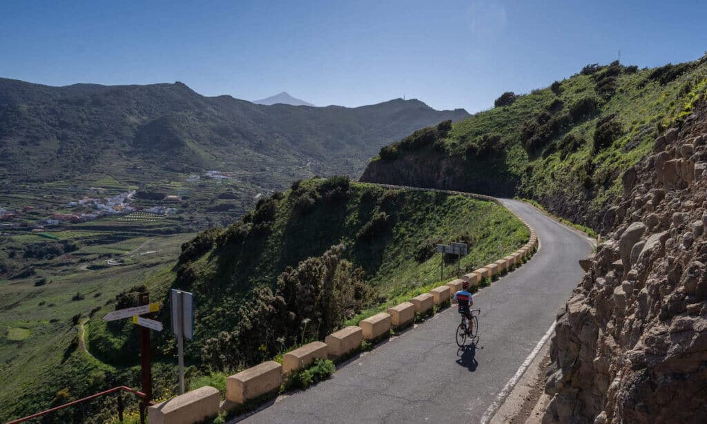 Cyclist on quiet paved road above valley and town on Tenerife in Canary Islands, Spain with mountain range in distance