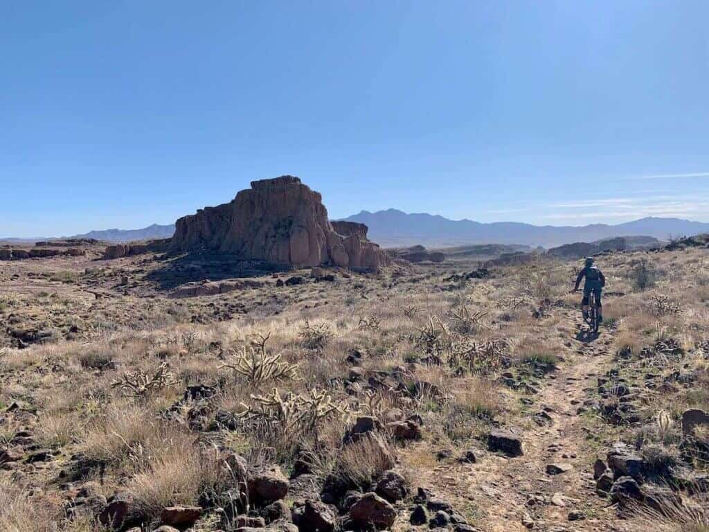 Mountain biker on rugged mountain bike trail in desert of Kingman, Arizona with tall rock monolith in the distance