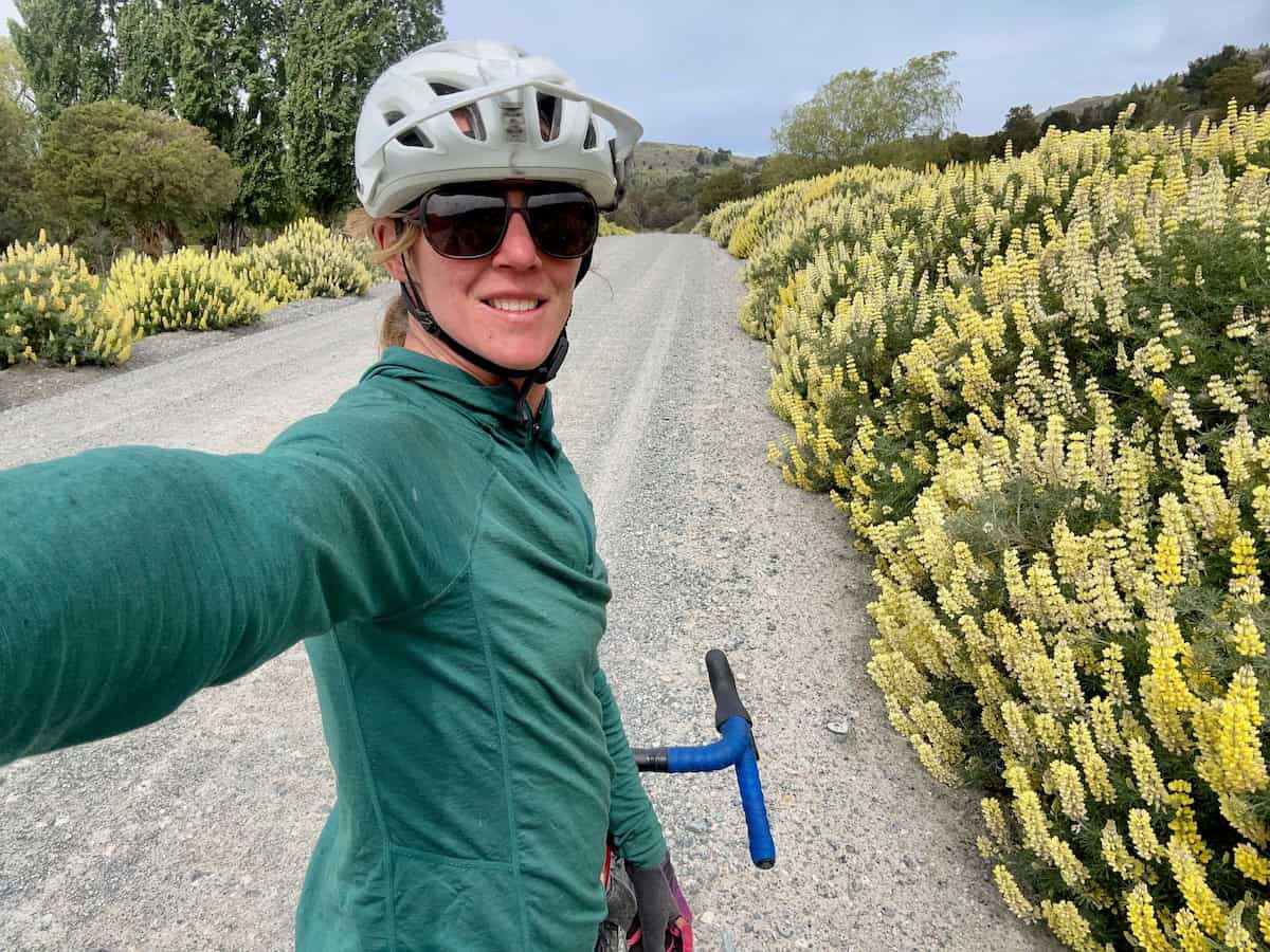 Female cyclist taking a selfie with blooming yellow lupines lining gravel road