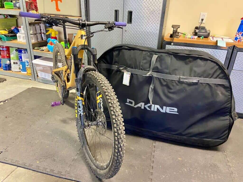Mountain bike leaning against Dakine bike bag in garage