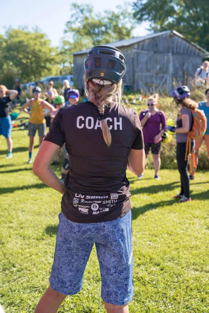 Back of woman mountain biker wearing coach jersey in front of group of women riders