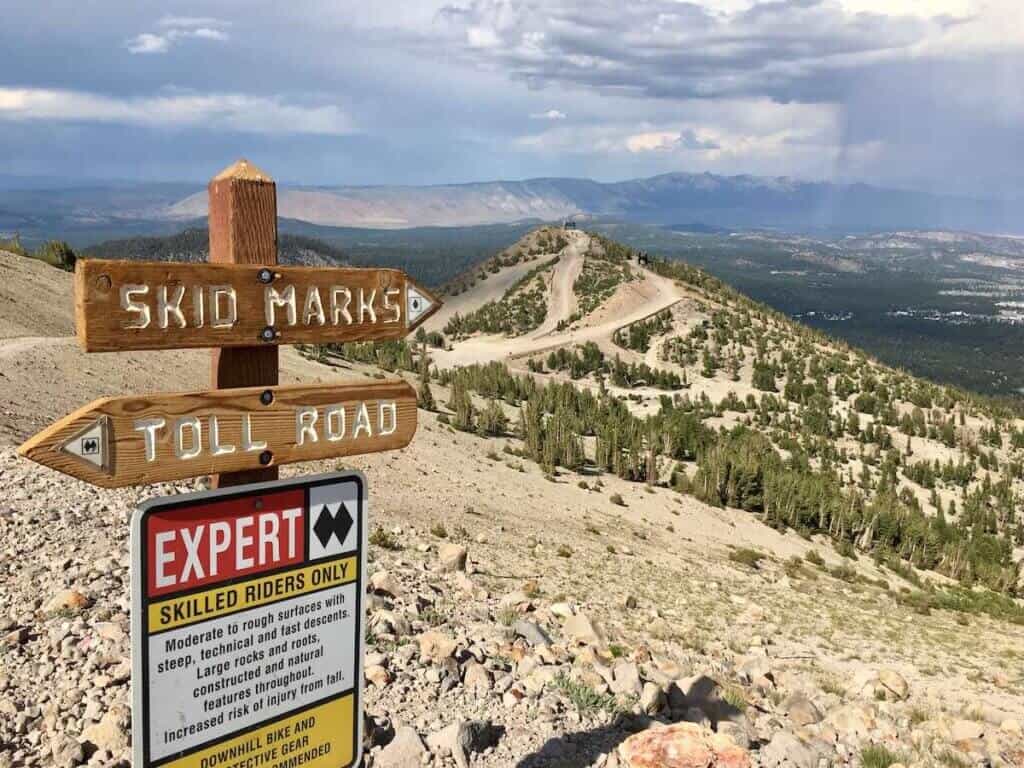 Trail sign at top of Mammoth Mountain Bike Park. Signs say "Skid Marks" "Toll Road" and "Expert Only"