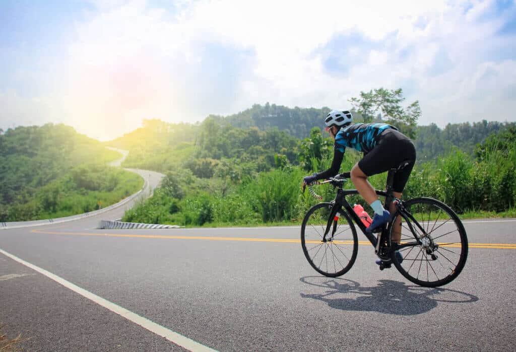 Road cyclist riding bike on empty road with sun rising over hills