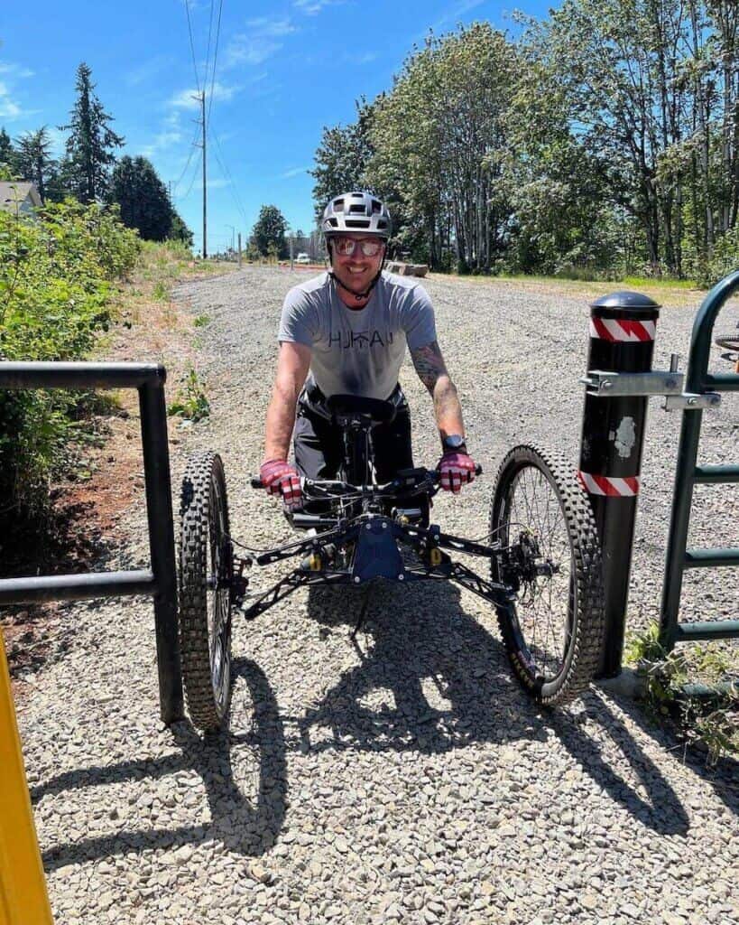 Jermey McGhee smiling for photo while riding three-wheeled adaptive mountain bike through metal gate
