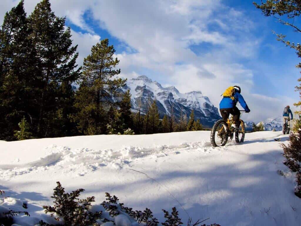 Person riding fat bike through the snow with snow-capped peaks in the distance
