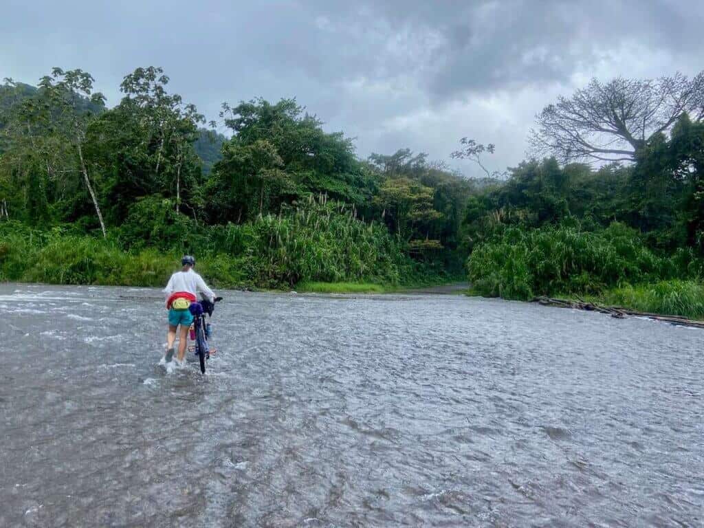 Bikepacking walking bike across shallow, wide river in Costa Rica