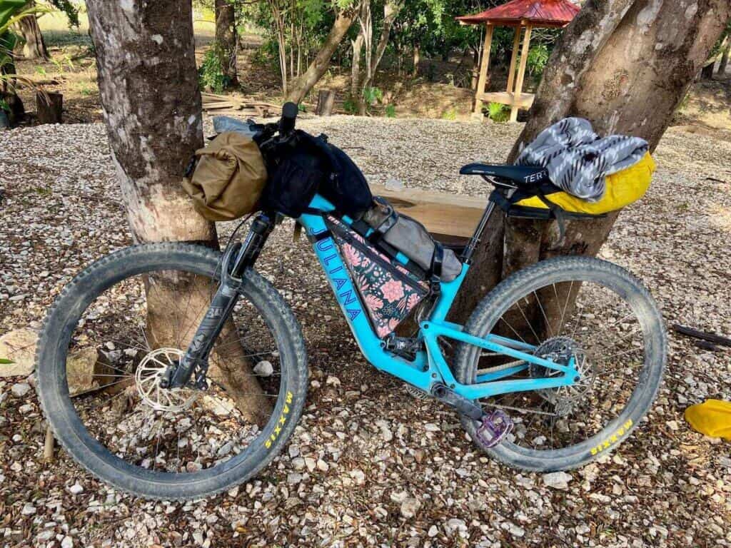 Sepeda gunung Juliana dimuati perlengkapan bikepacking dan bersandar di pohon