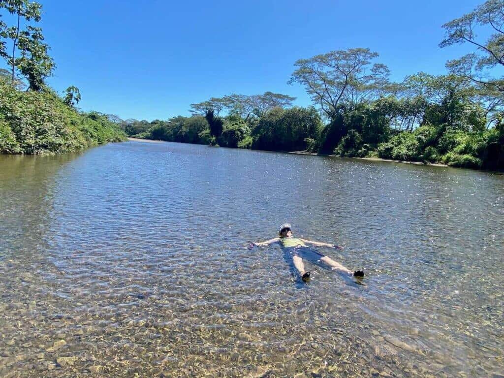 Woman lying in shallow river wearing all her bike clothes and gear to cool off in Costa Rica