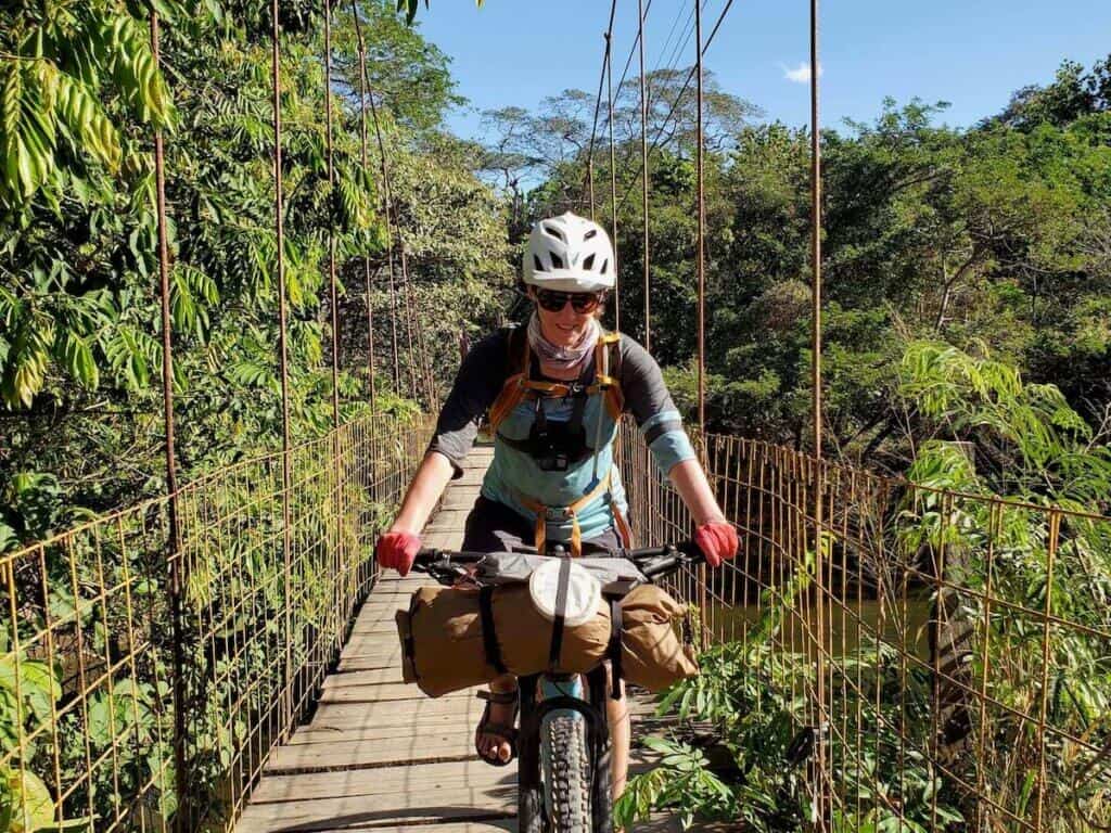 Woman riding loaded bikepacking bike over suspension bridge in Costa Rica