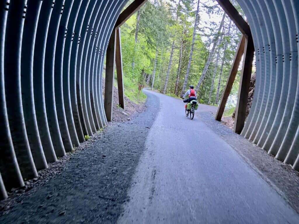 Bikepacking riding bike through tall, round metal tunnel on Olympic Discovery Trail in Washington 