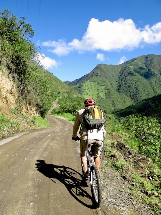 Cyclist riding bike on dirt road in Ecuador surrounded by lush, green mountains