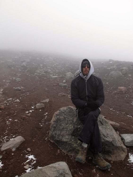 Man sitting on rock in misty, cloudy terrain of Chimborazo Volcano in Ecuador
