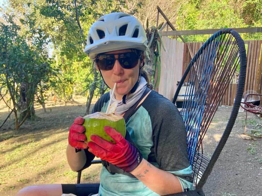 Becky wearing Ombraz Sunglasses and mountain bike helmet sipping on fresh coconut with a straw in Costa Rica