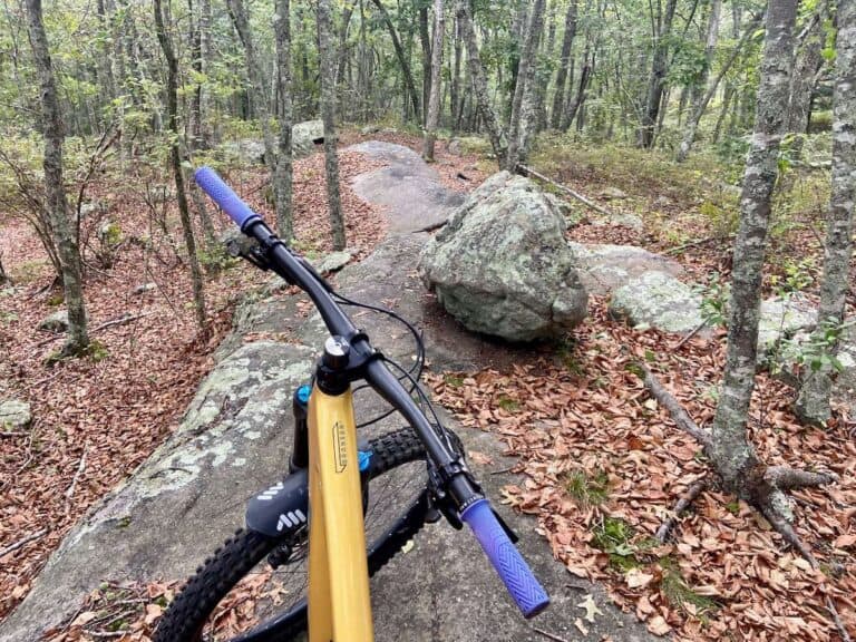 Photo out over front handlebars of bike on narrow rock slab trail in Woody Hill trail network in Rhode Island