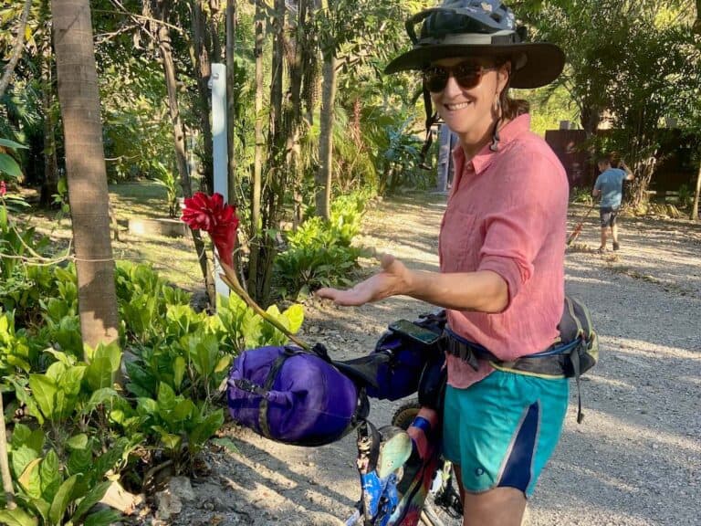 Woman standing next to loaded bikepacking bike pointing at flower sticking out of Rogue Panda seat post bag