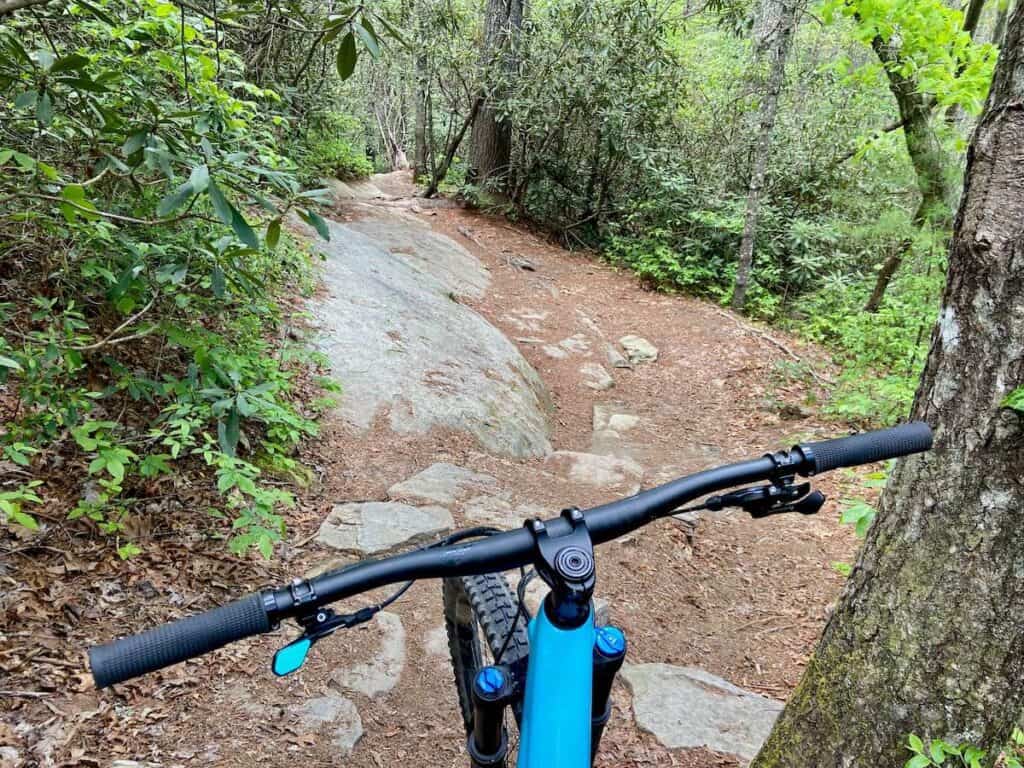 Photo out over front of mountain bike handlebars onto rock section of singletrack trail in DuPont State Forest in Brevard