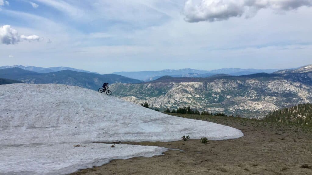 Mountain biker trying to ride bike down big snow pile on top of Mammoth Mountain Bike Park in California