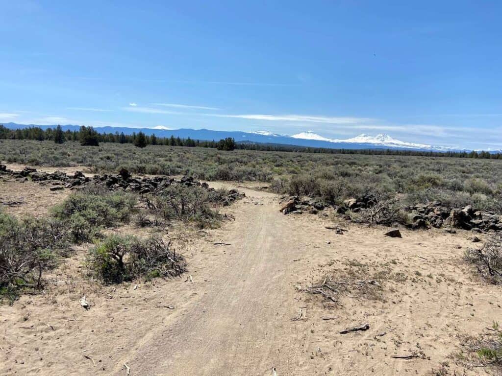 Singletrack mountain bike trail through scrub brush landscape at Maston Trail System in Oregon with snow-capped mountains in far distance