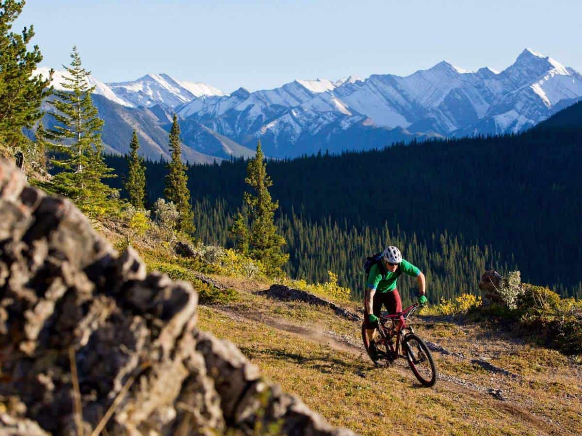 Man riding bike on scenic trail with tall snow-capped Rocky Mountains behind him