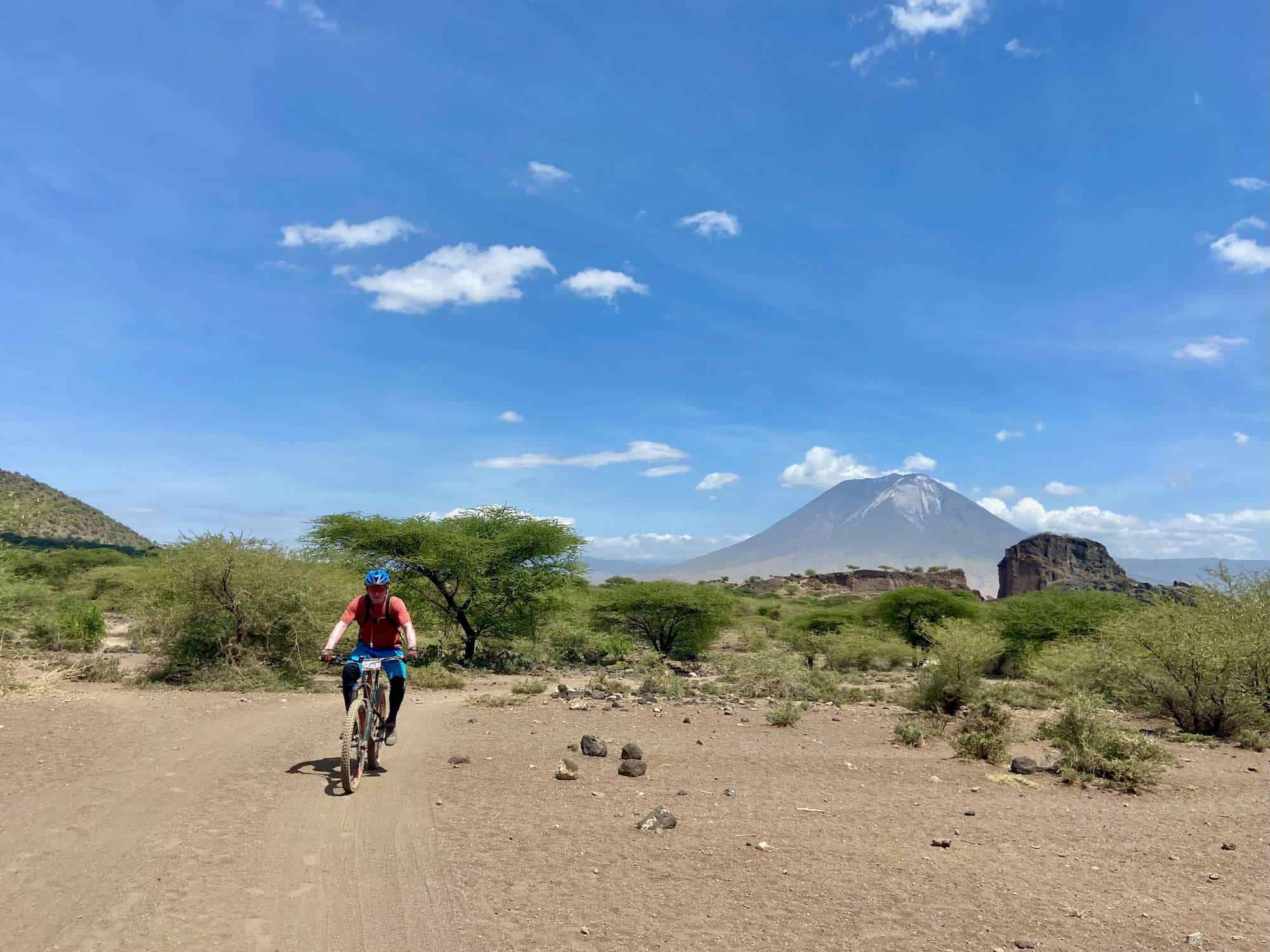 Man riding mountain bike on dirt road in remote during K2N Stage Race in Tanzania with tall volcano in background
