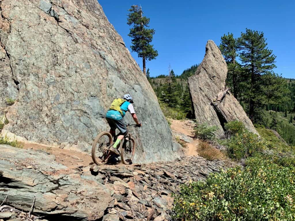 Mountain biker riding bike down loose and rocky section on trail lined with tall rock boulders