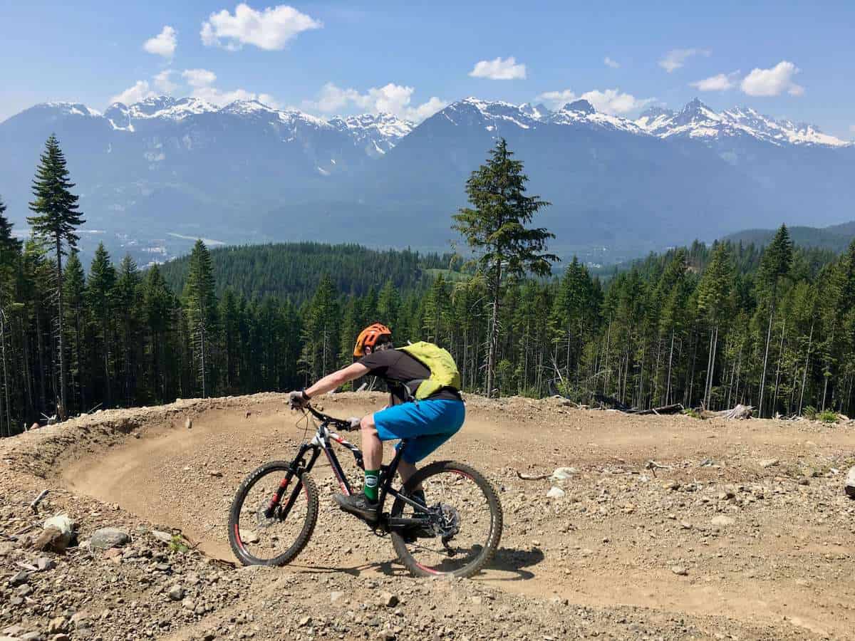 Mountain biker riding around big bermed dirt turn in Squamish, British Columbia with snow-capped mountains in distance