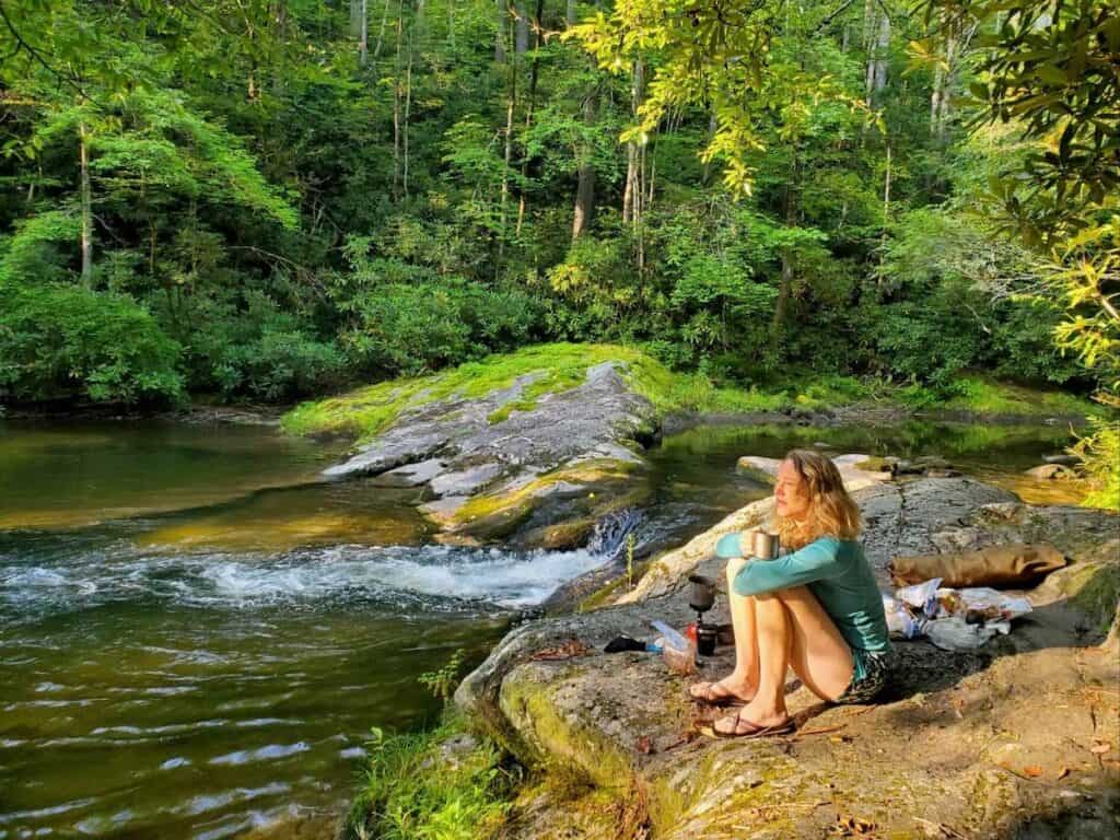 Woman sitting on rock by very scenic river in North Carolina with early morning sun casting a glow over her
