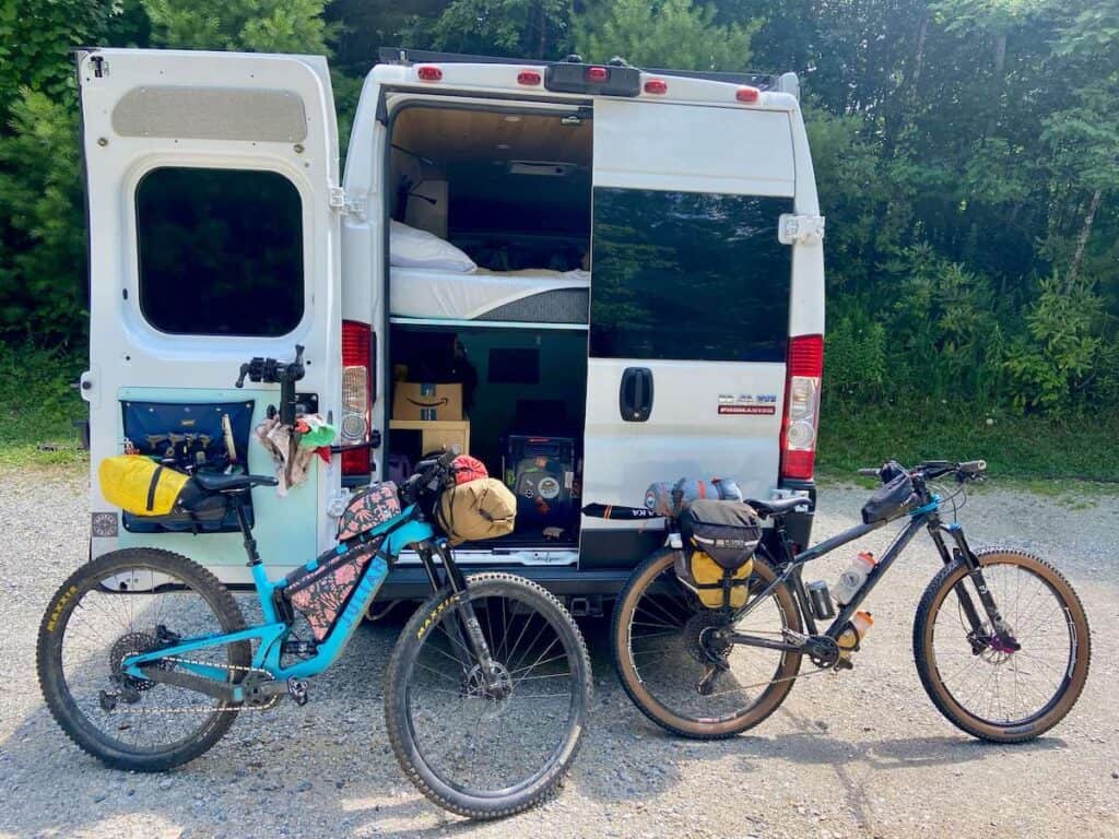 Two mountain bikes loaded with bikepacking bags leaning against the back of converted campervan