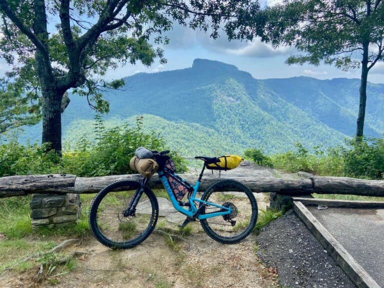 Mountain bike loaded with bikepacking gear leaning against fence with dramatic North Carolina landscape as backdrop
