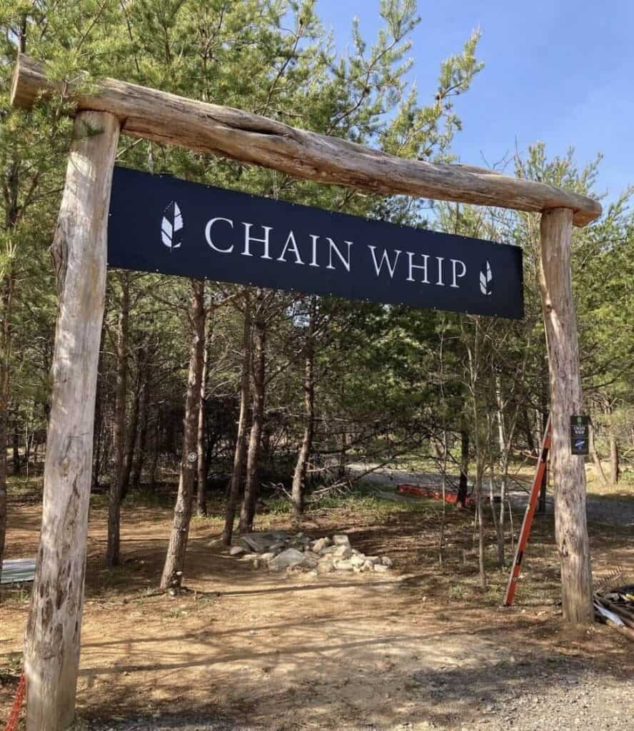 Image of a wooden gate over trail with a sign that reads "chain whip" in the middle of a forest at Chestnut Mountain Nature Park in North Carolina