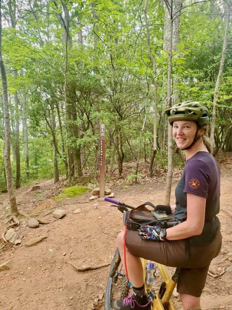 Woman sitting on mountain biking smiling for camera before dropping into mountain bike trail in North Carolina