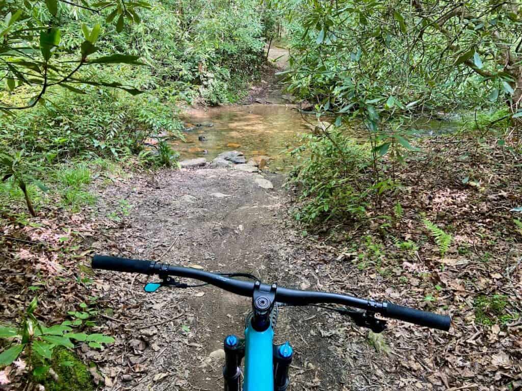 Photo out over front of mountain bike handlebars on to trail and river crossing in North Carolina