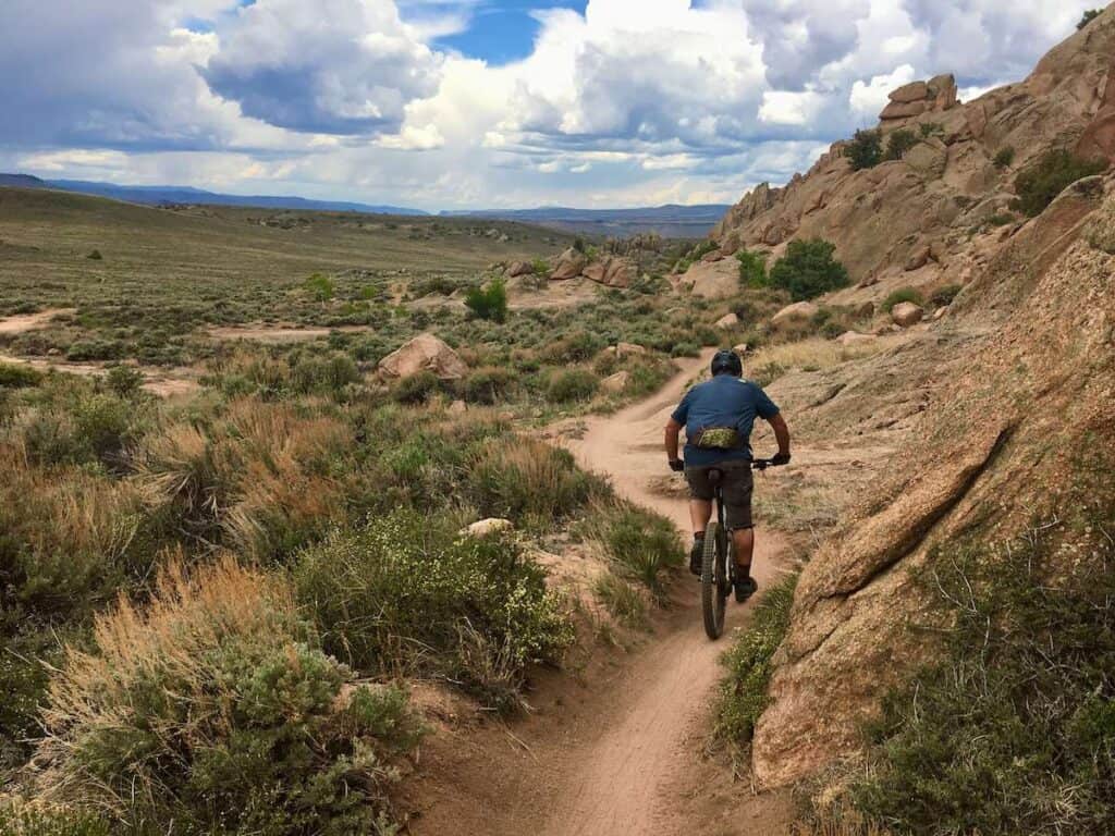 Mountain biker riding bike down singletrack trail in Hartman Rocks, Colorado with large rock boulders on right side